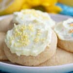 Titled image close up of frosted Keto Lemon Sugar Cookies on a white plate over a teal patterned napkin.