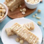 Two keto protein bars on a white plate with macadamia nuts and white chocolate chips in the background.