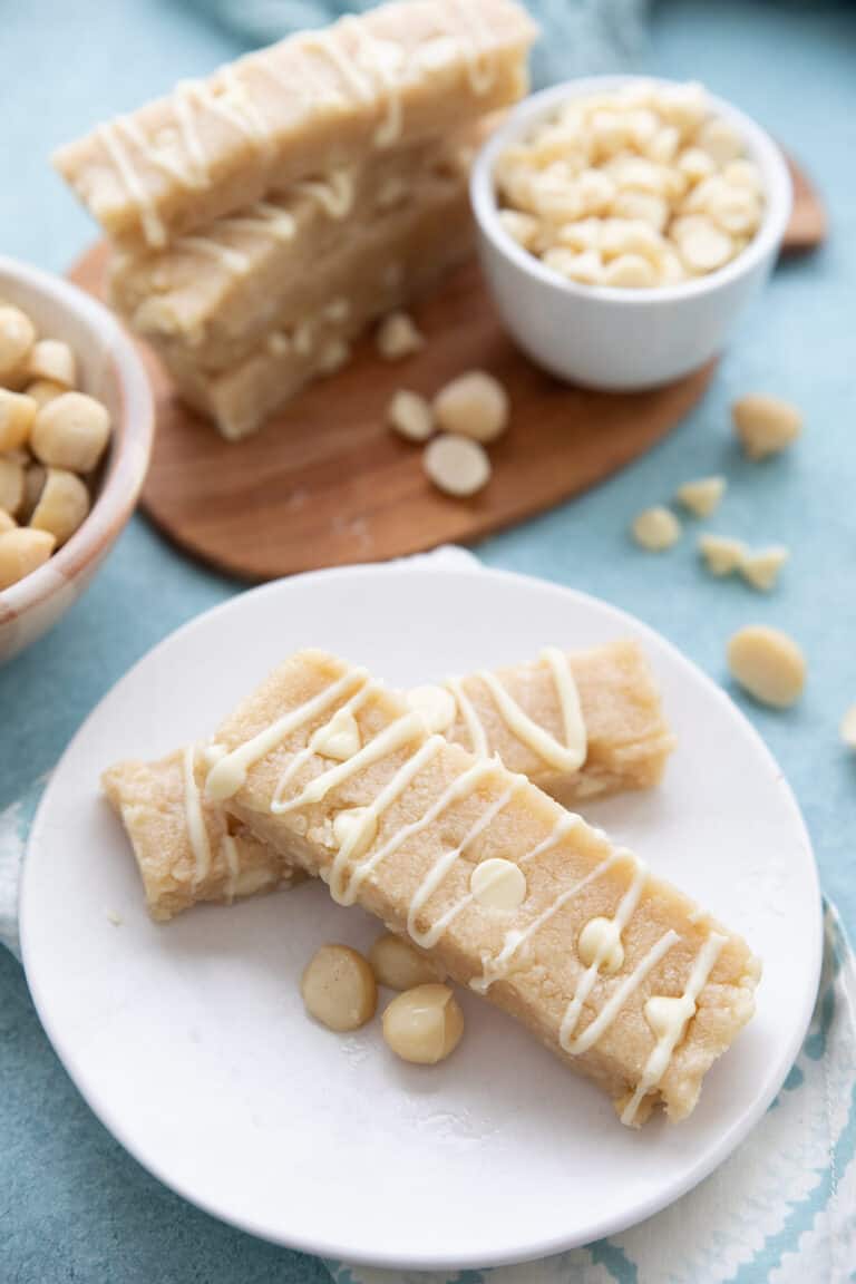 Two keto protein bars on a white plate with macadamia nuts and white chocolate chips in the background.