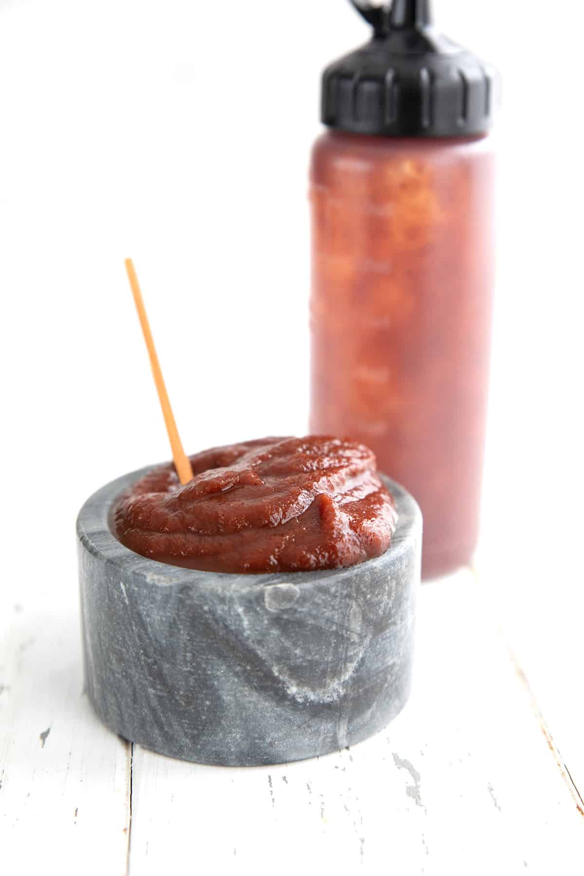 A bowl of keto ketchup in front of a squeeze bottle of more ketchup.