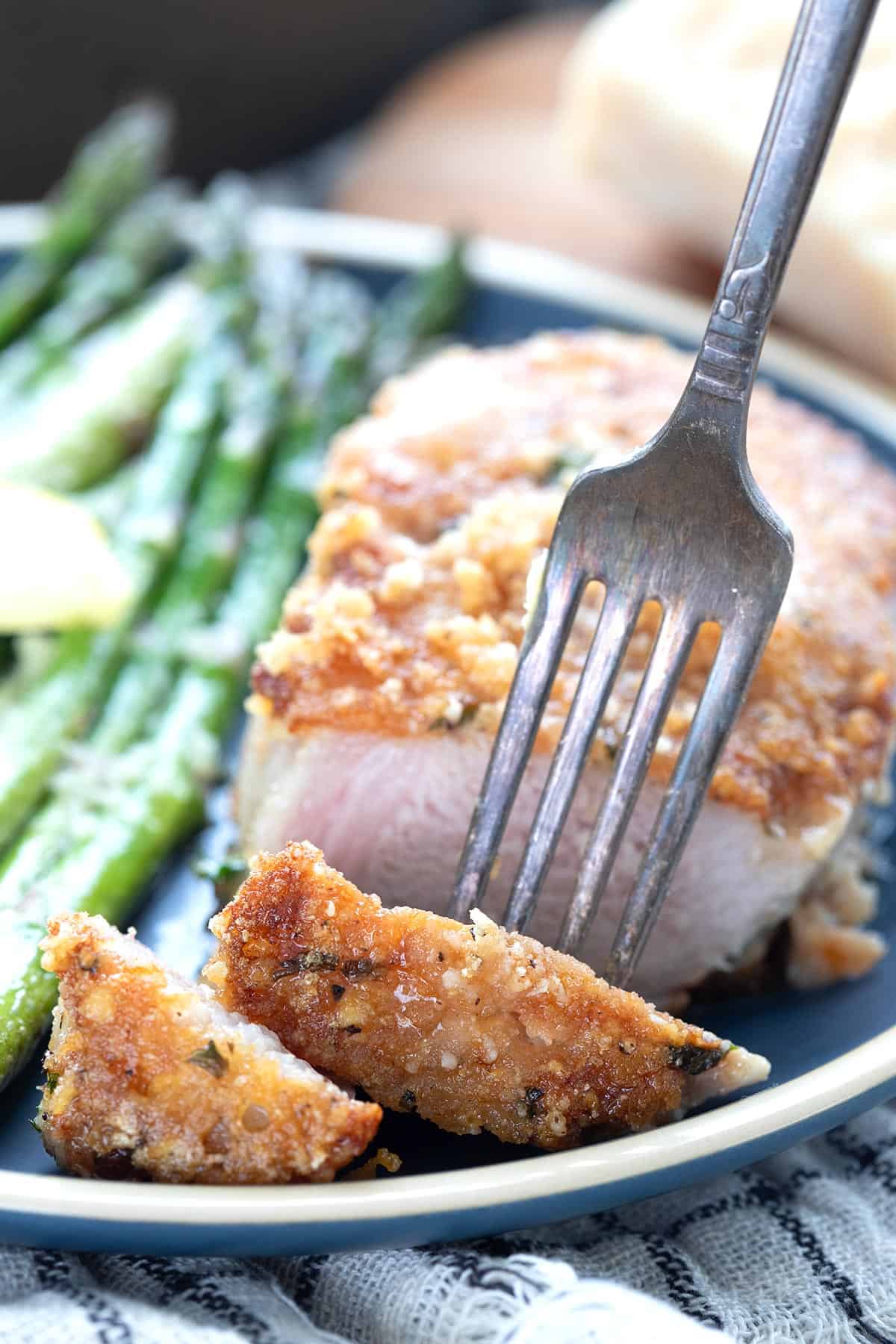 A fork digging into a sliced keto pork chop on a blue plate.
