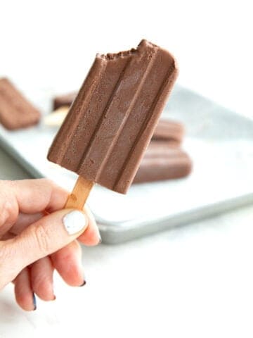 A hand holding up a sugar free fudge pop with a bite taken out of it.