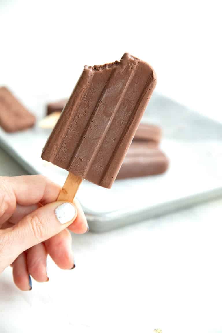 A hand holding up a sugar free fudge pop with a bite taken out of it.