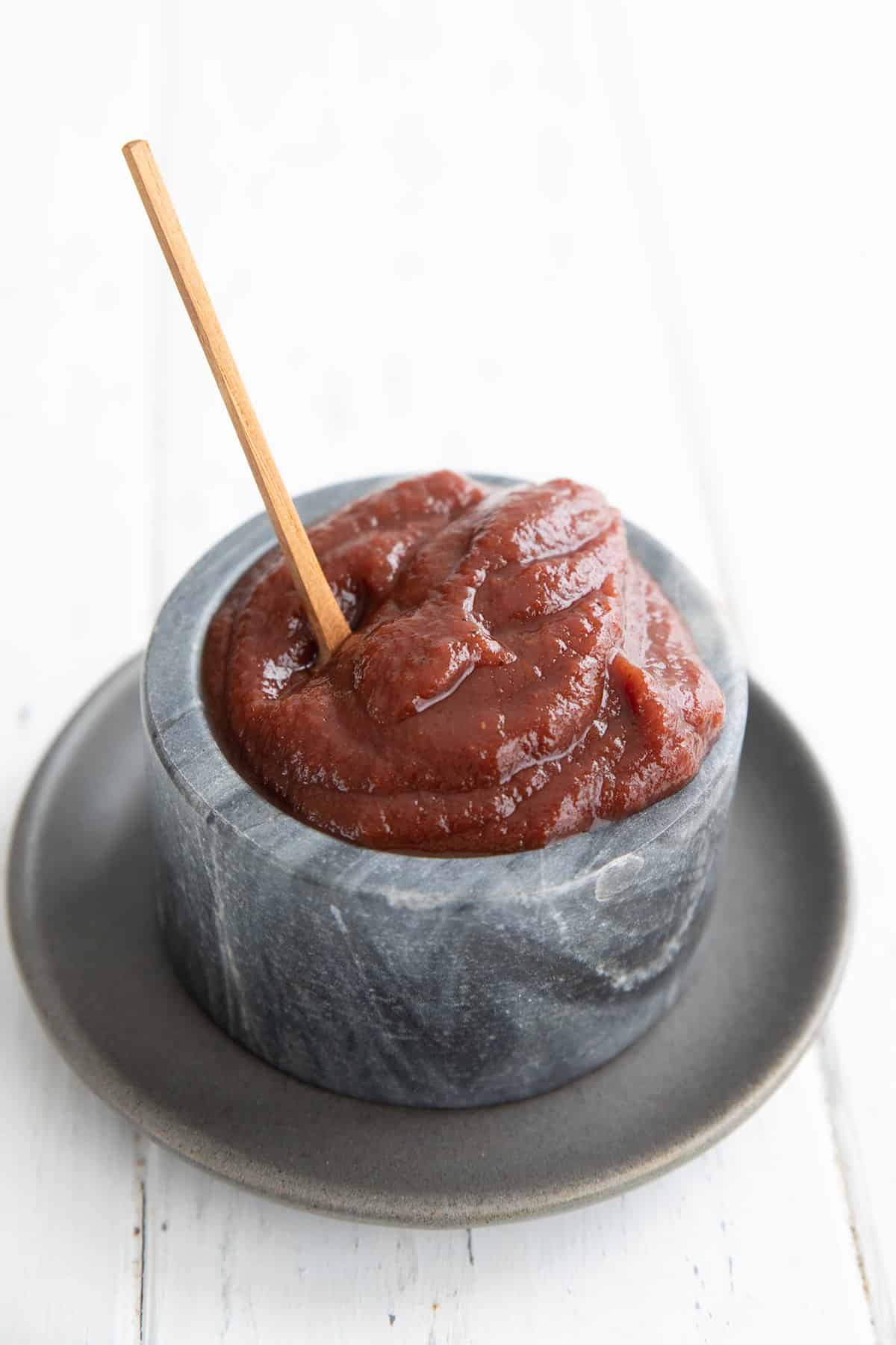Sugar Free Ketchup piled up in a gray marble bowl with a small wooden spoon sticking out.