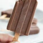A hand holding up a sugar free fudgesicle with a bite taken out of it.