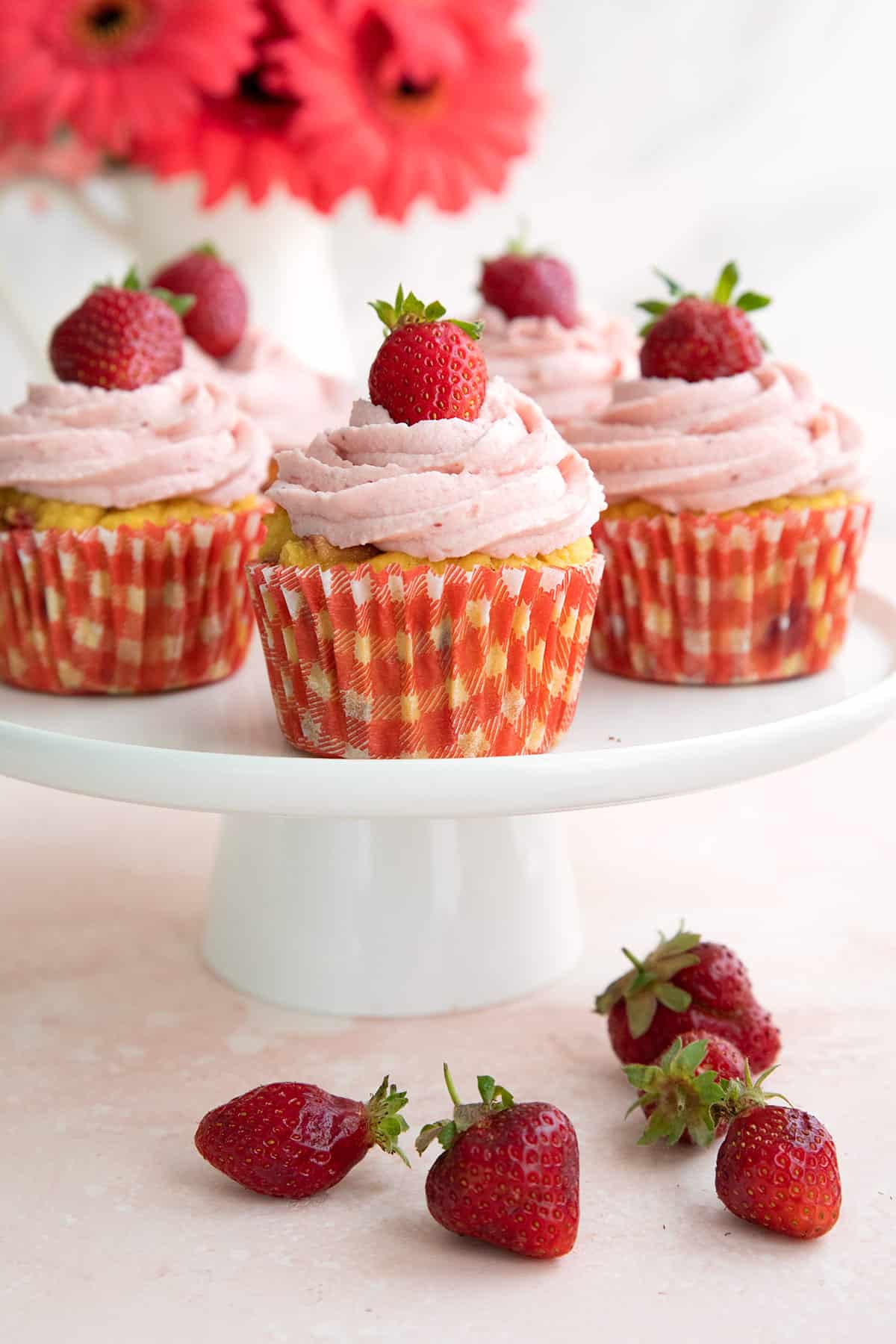Keto Strawberry Cupcakes on a white cake stand with flowers in the background.