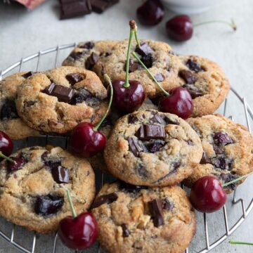 Keto Cherry Chocolate Chunk Cookies on a cooling rack with a bowl of cherries in the background.