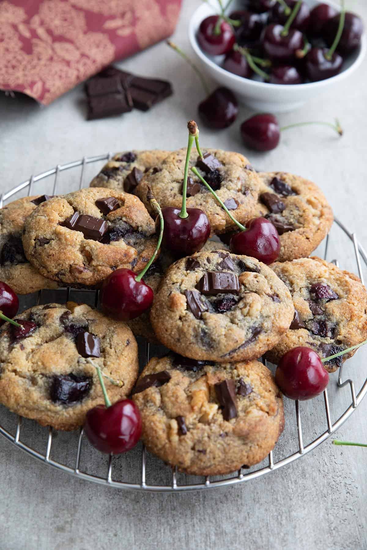 Keto Cherry Chocolate Chunk Cookies on a cooling rack with a bowl of cherries in the background.