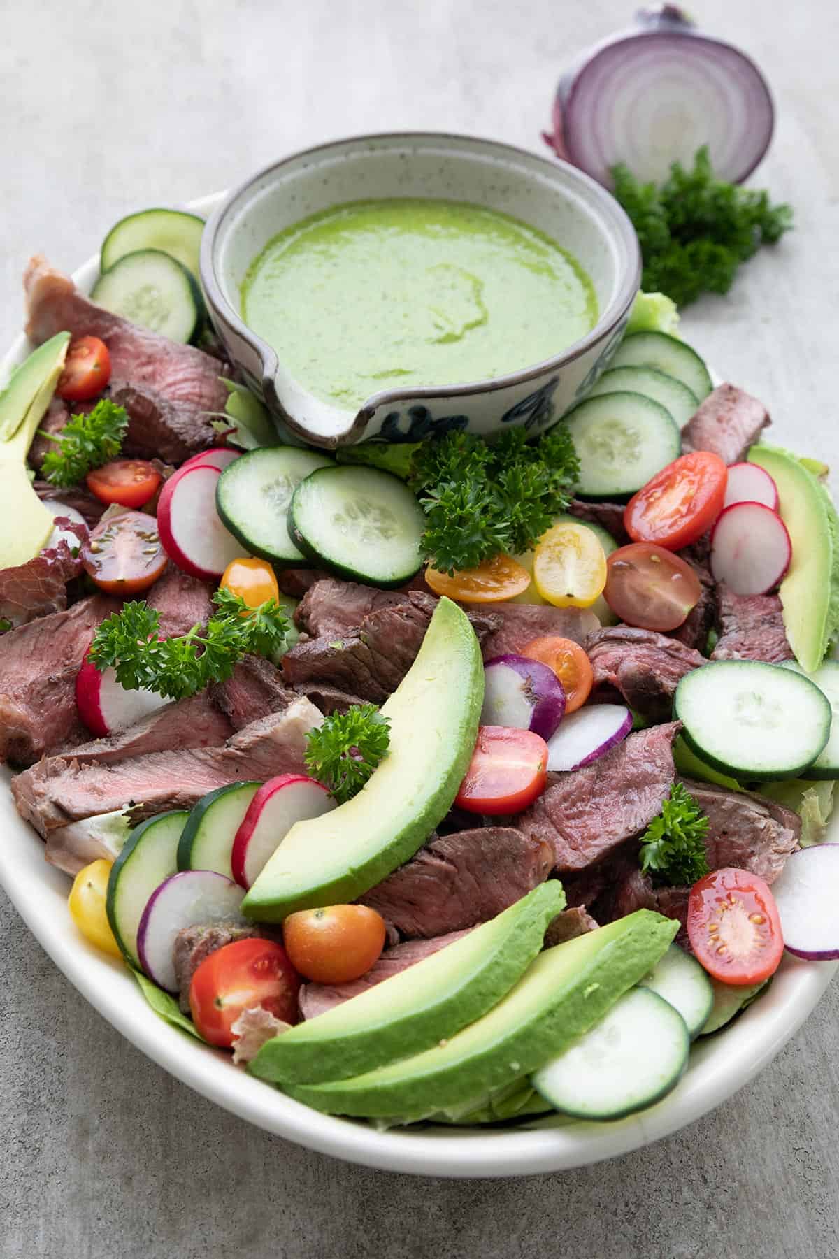 An oval platter filled with steak salad and chimichurri.