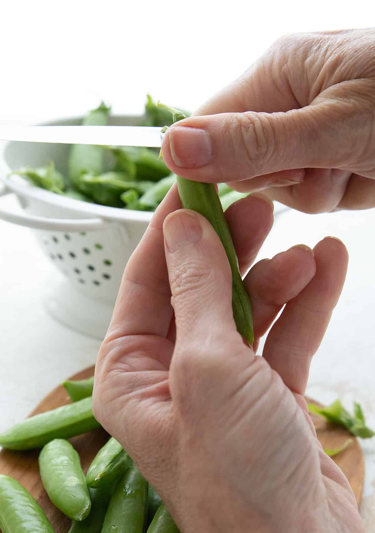 Two hands showing how to trim sugar snap peas.