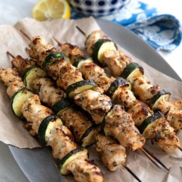 Chicken Souvlaki skewers on a paper lined tray with cauliflower rice in the background.