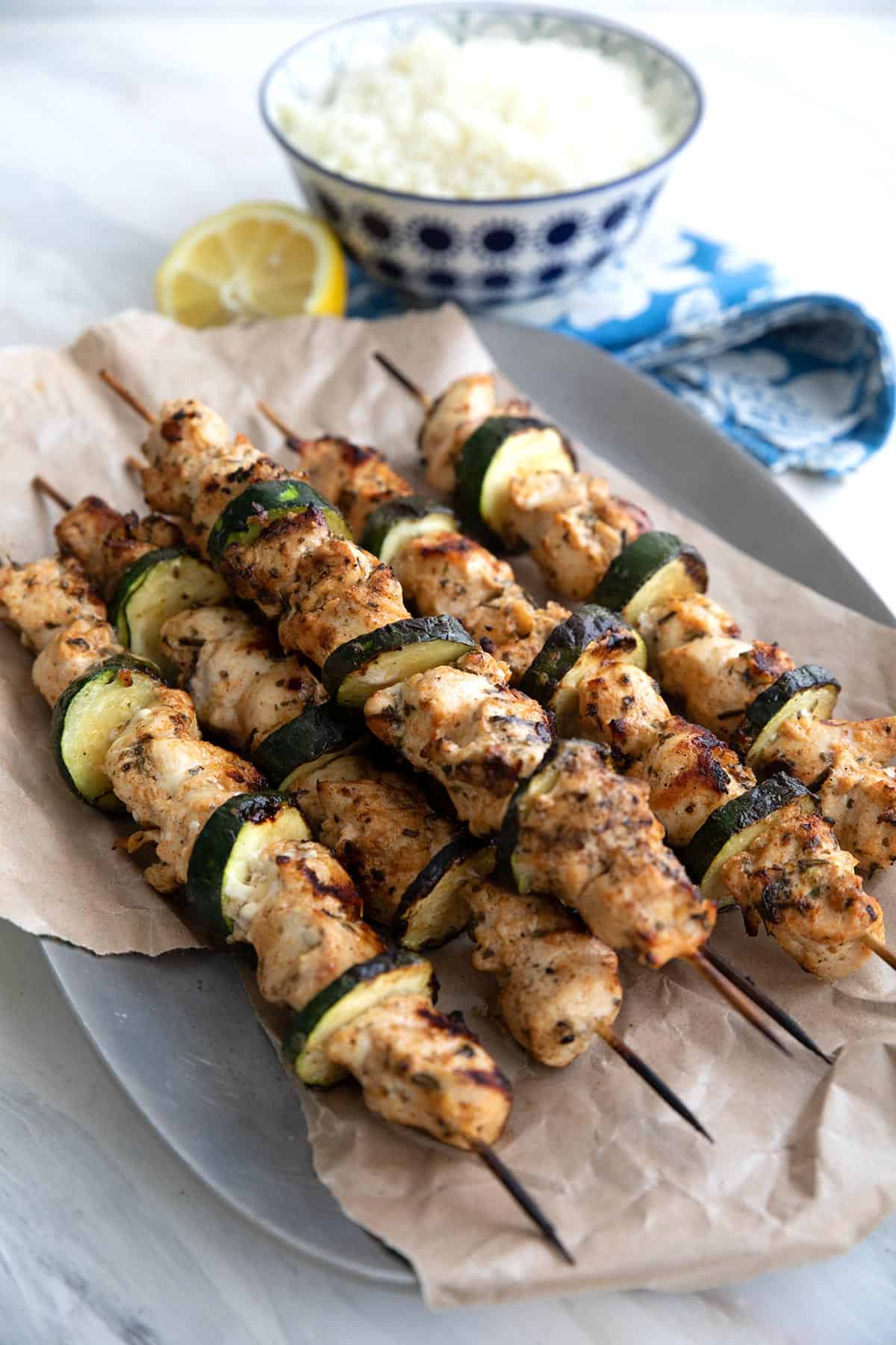 Chicken Souvlaki skewers on a paper lined tray with cauliflower rice in the background.