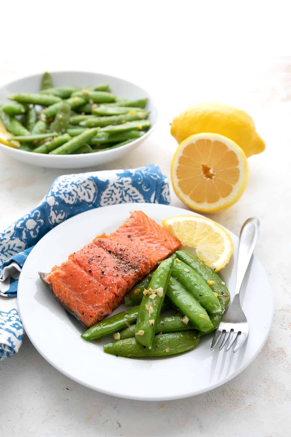 A white plate with salmon and cooked sugar snap peas.