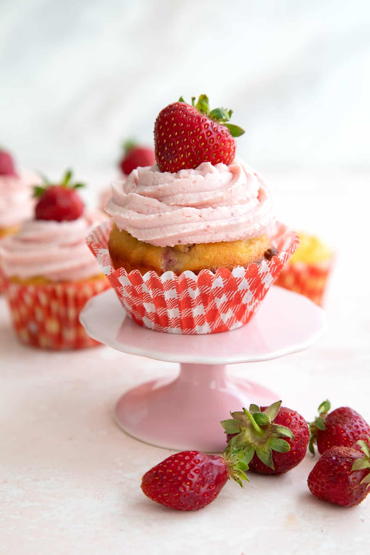 A low carb strawberry cupcake on a pink cupcake stand in front of some fresh berries.