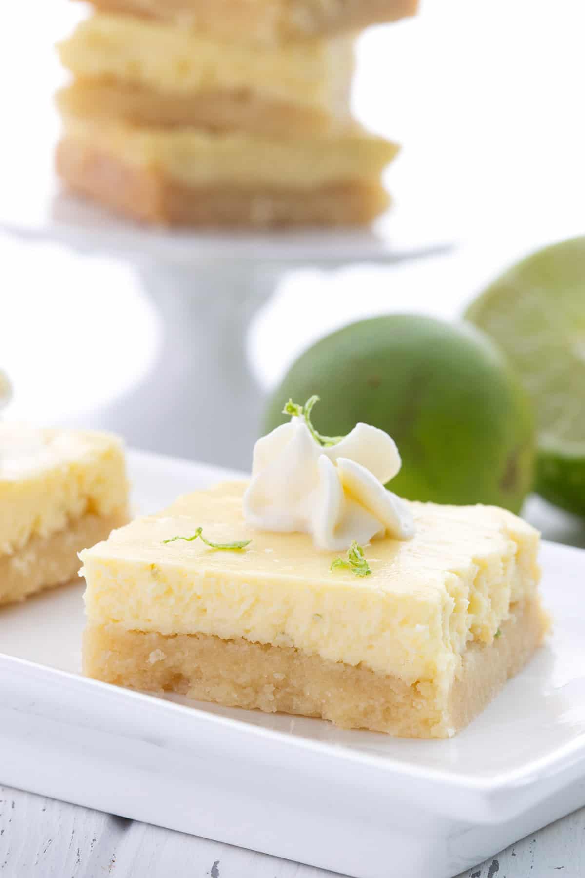 A low carb key lime bar on a white tray in front of limes and more bars.
