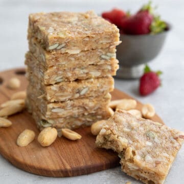 A stack of keto peanut butter granola bars on a wooden cutting board with peanuts strewn around.