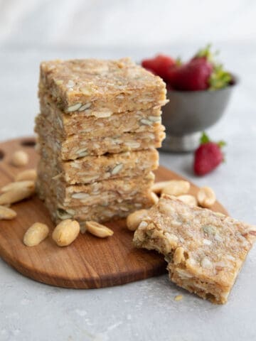 A stack of keto peanut butter granola bars on a wooden cutting board with peanuts strewn around.