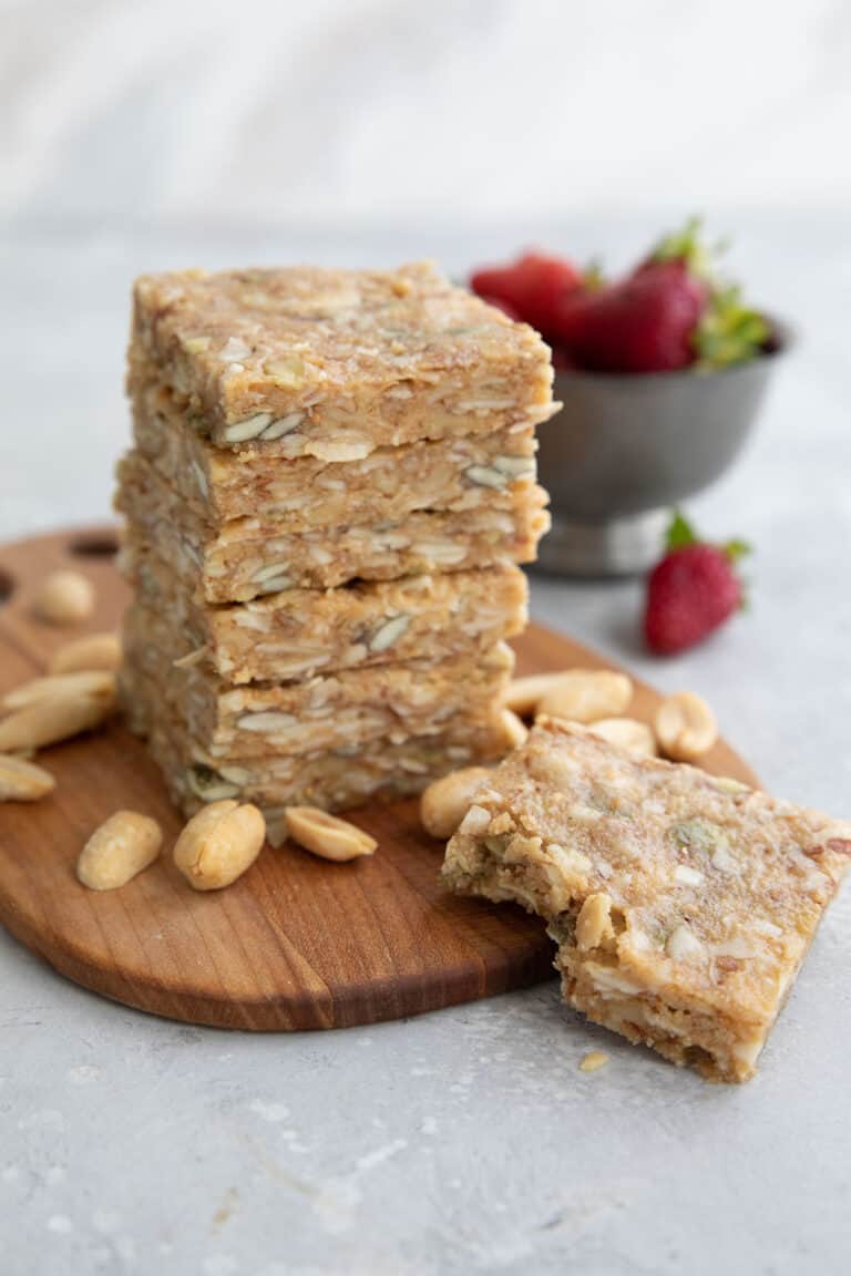 A stack of keto peanut butter granola bars on a wooden cutting board with peanuts strewn around.