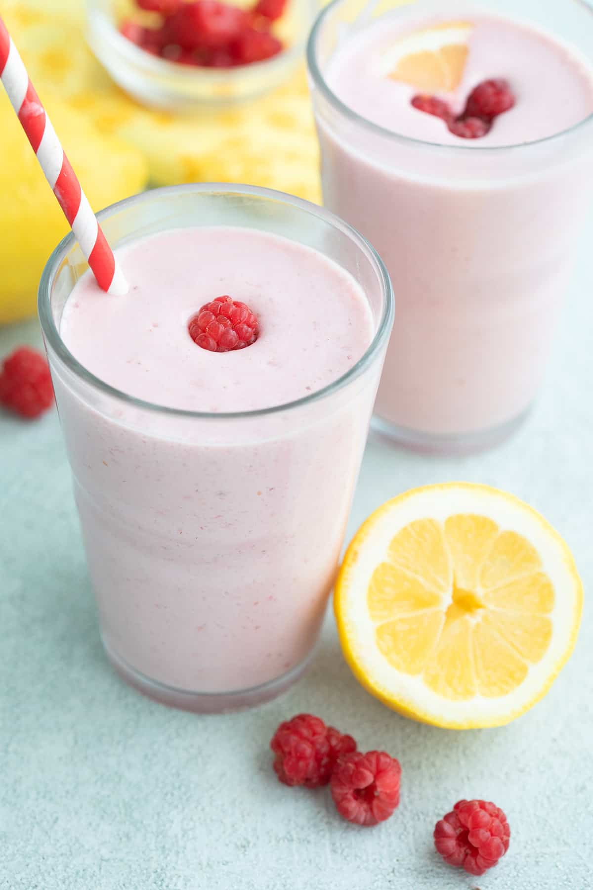 Two raspberry keto protein shakes on a table with lemon and raspberries.
