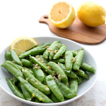 Sautéed sugar snap peas with lemon and garlic in a white serving dish.