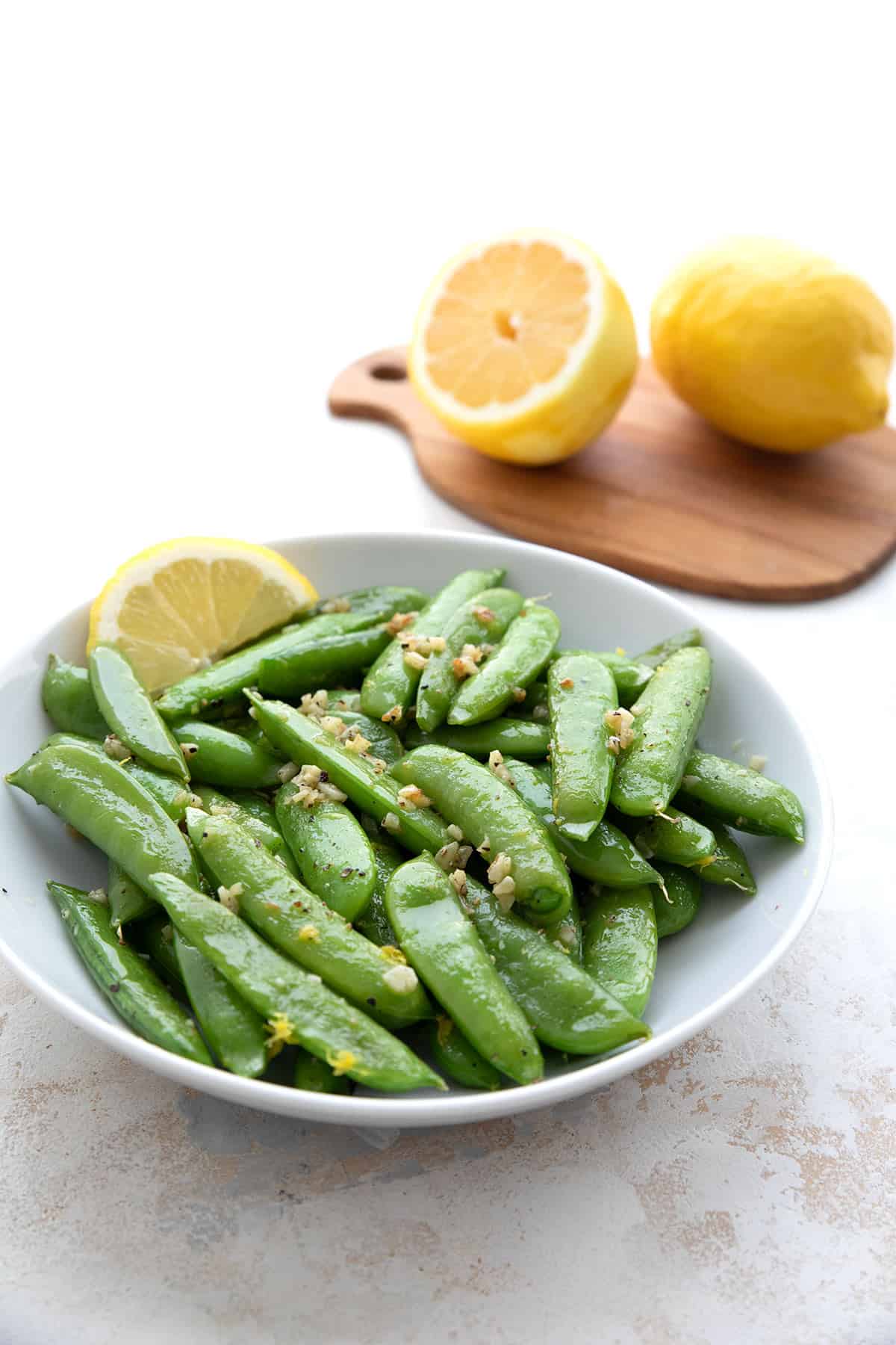 Sautéed sugar snap peas with lemon and garlic in a white serving dish.