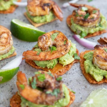 Guacamole shrimp bites on a metal baking tray with slices of lime.