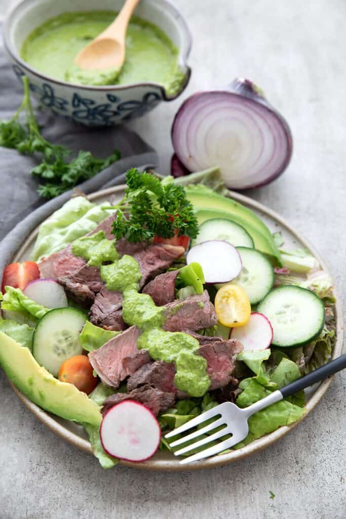 Chimichurri Steak Salad on a plate with onion and chimichurri in the background.