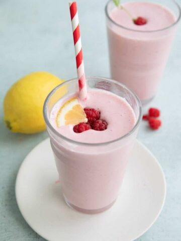 A glass of keto protein shake with a red striped straw and raspberries on top.