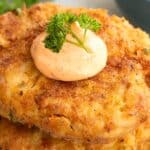 Titled image close up of a stack of three keto crab cakes with cajun mayo and a parsley sprig on top.