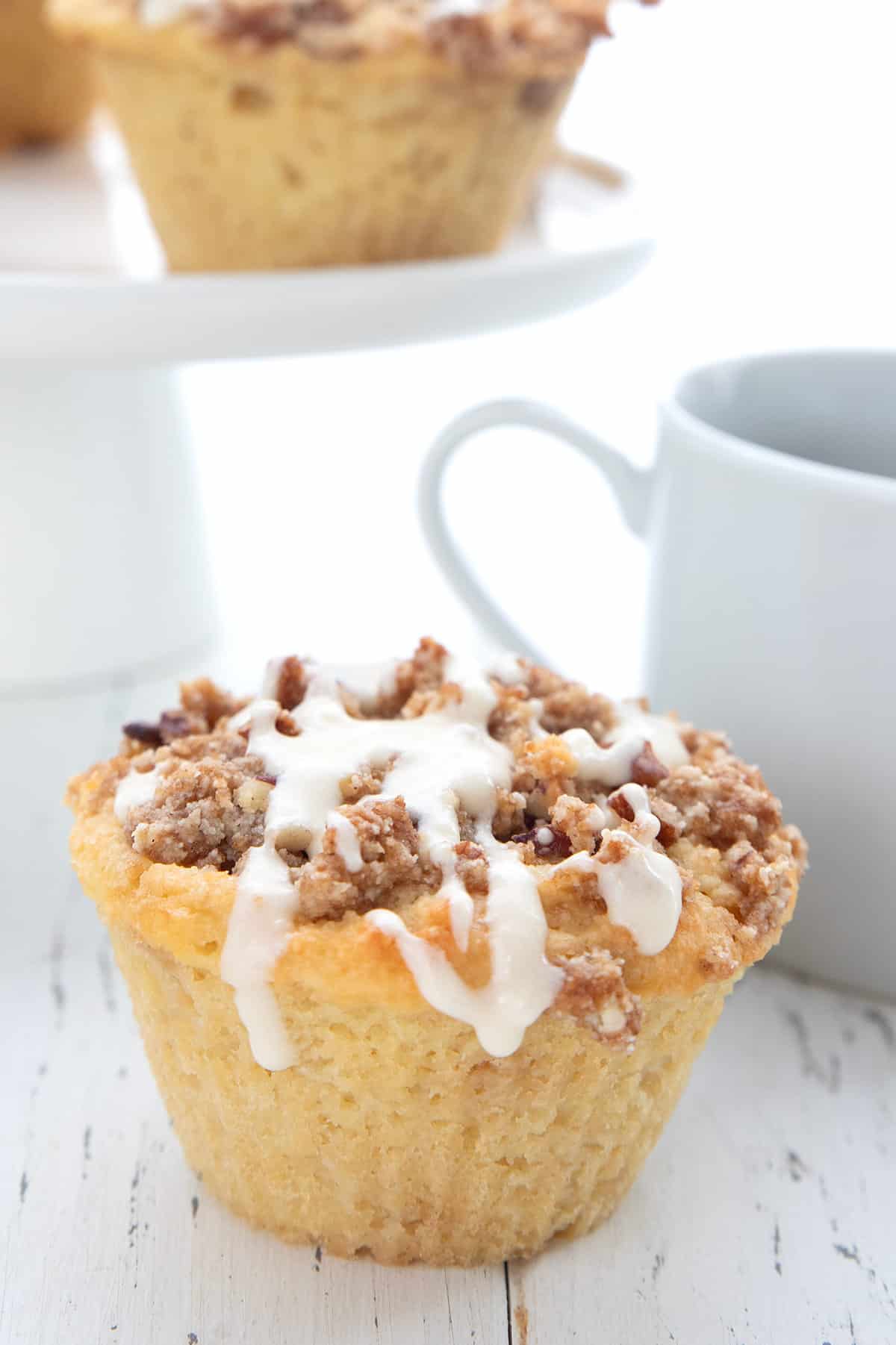 A keto muffin with crumb topping and vanilla drizzle on a white wooden table.