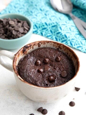 Easy keto protein mug cake in a coffee mug with chocolate chips on the table.