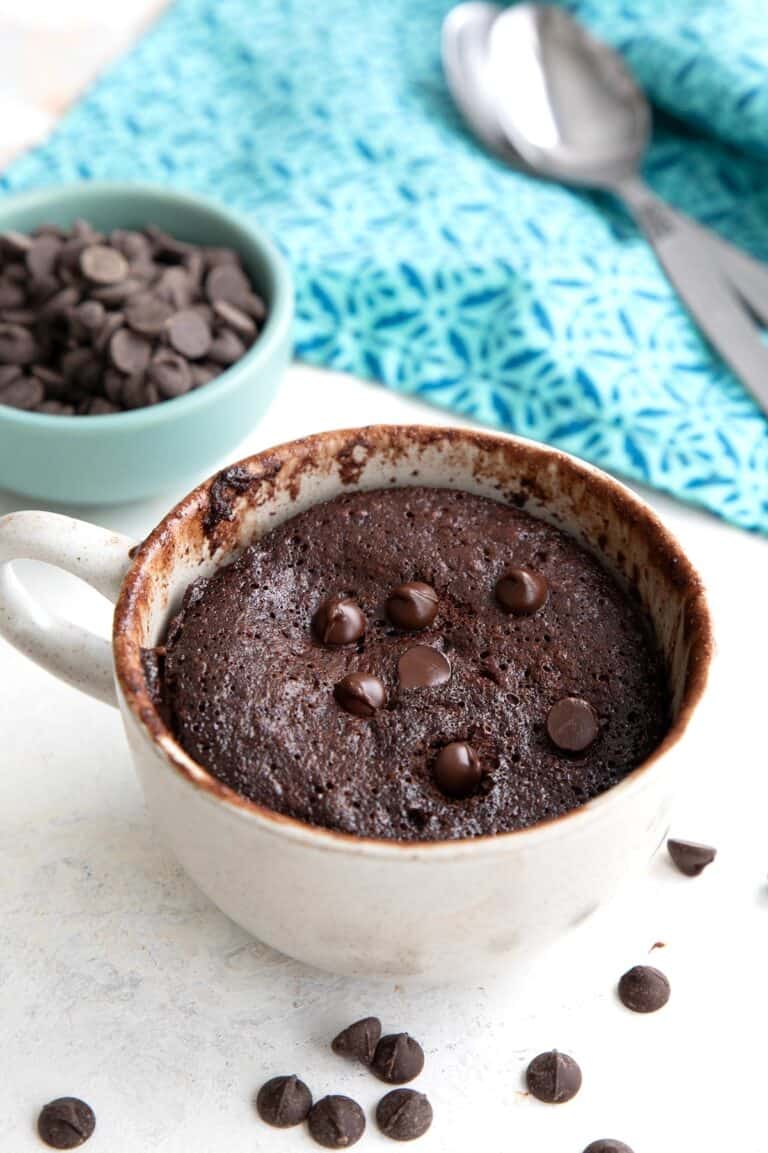 Easy keto protein mug cake in a coffee mug with chocolate chips on the table.