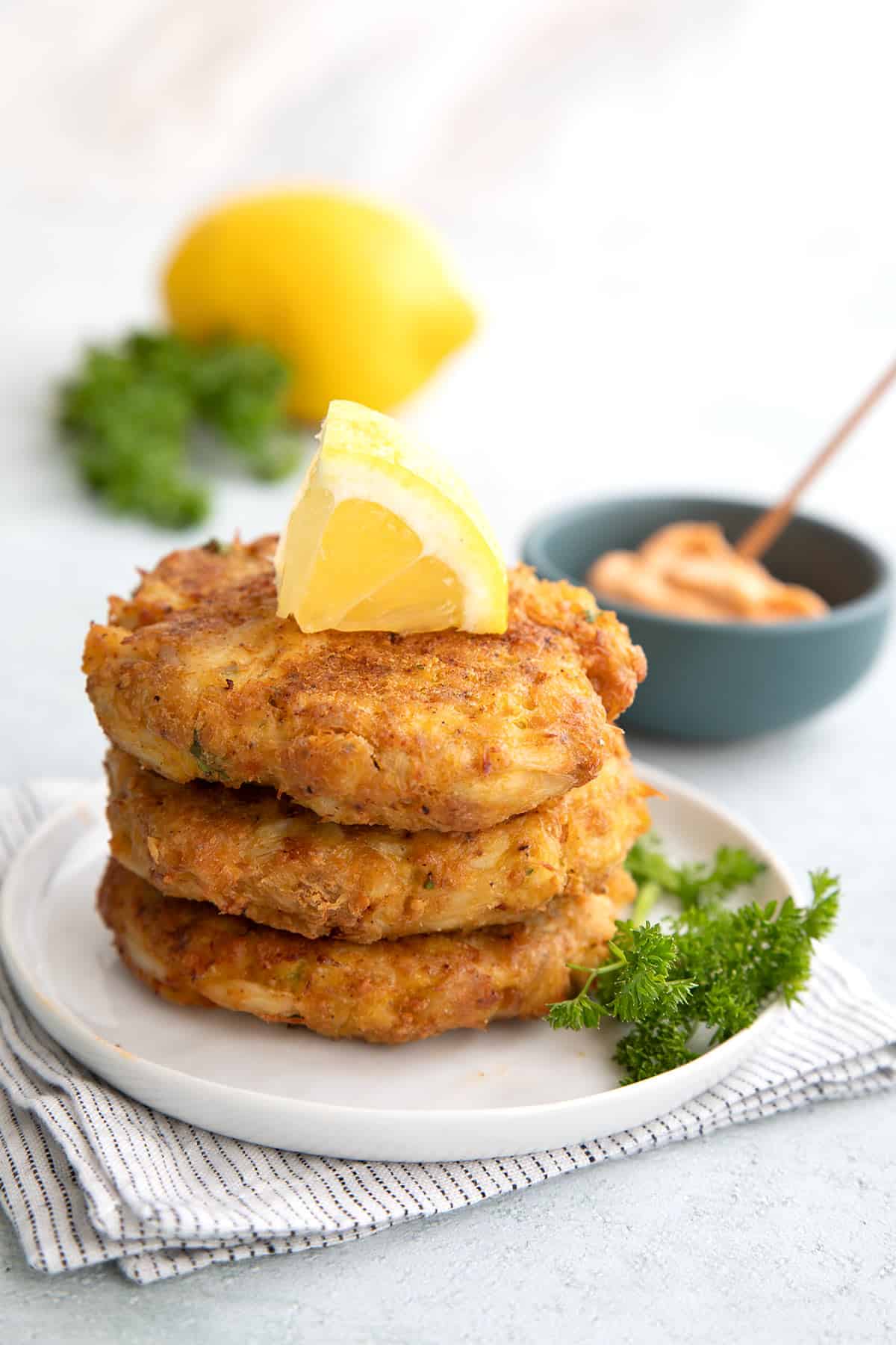 A stack of keto air fryer crab cakes on a plate with a slice of lemon on top.