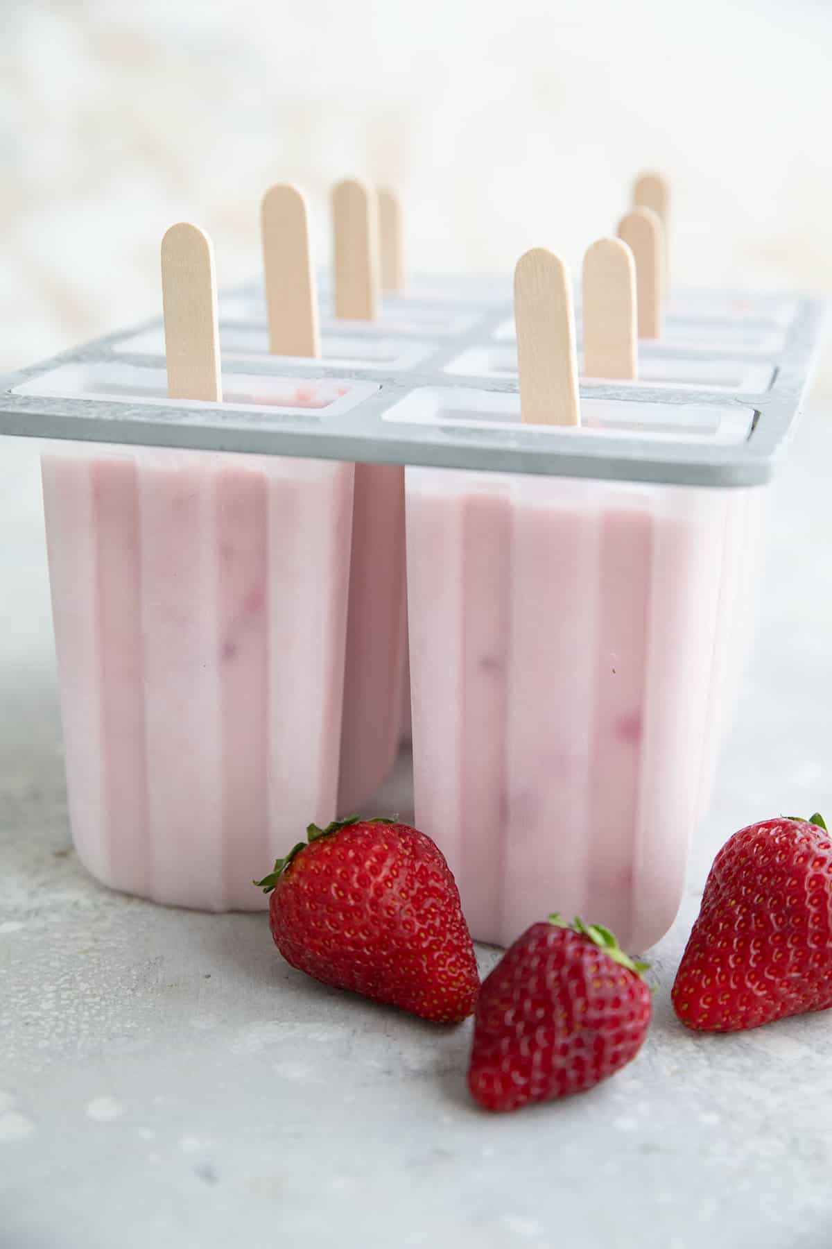 Strawberry Cheesecake Popsicles in the popsicle mold with fresh berries in front.