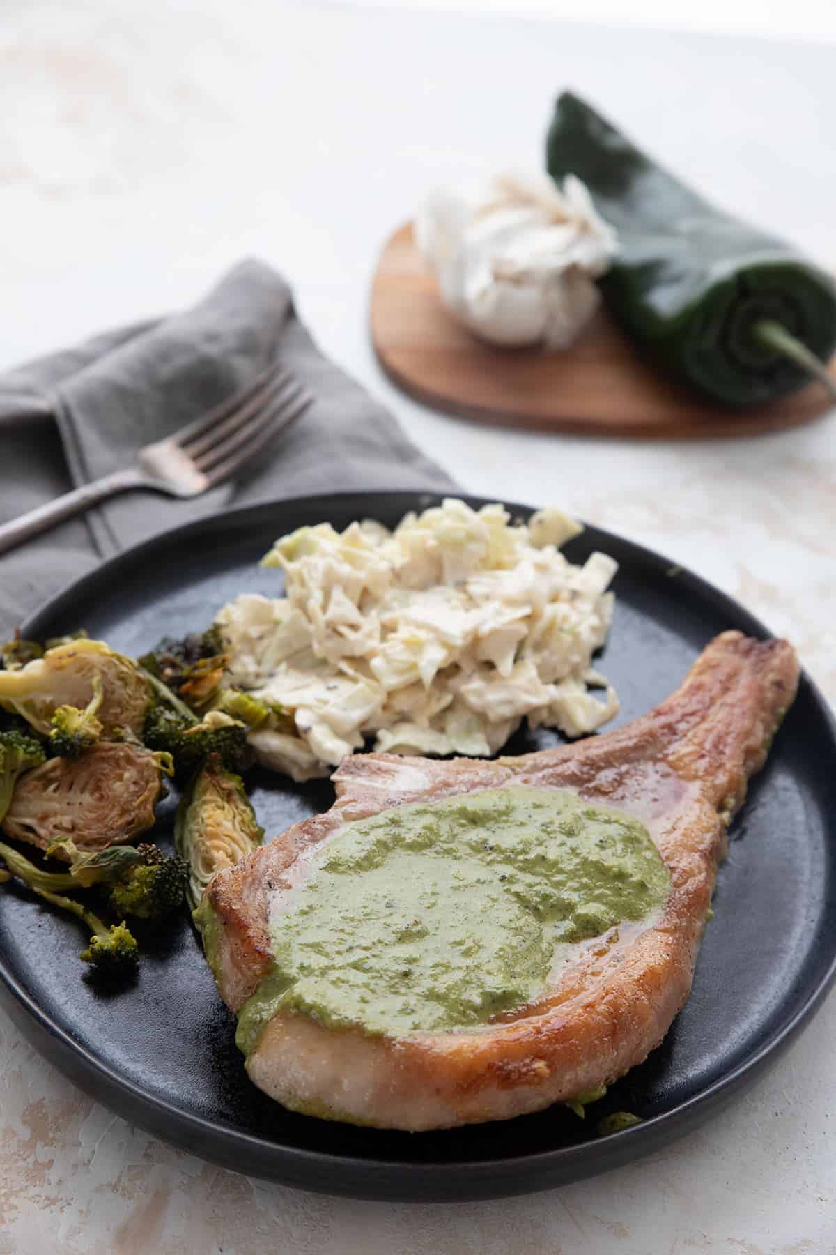 A pork chop topped with poblano sauce on a black plate.