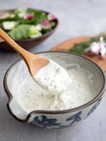 A wooden spoon lifting some feta dressing out of a grey patterned bowl.