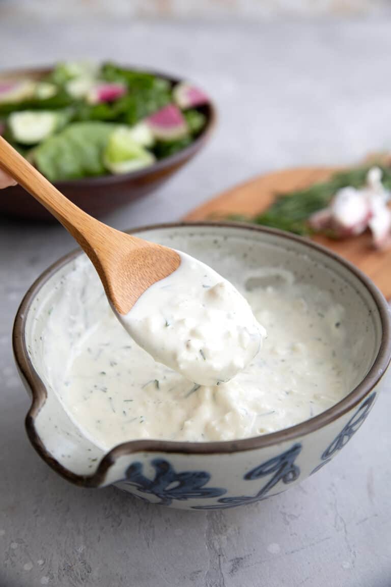 A wooden spoon lifting some feta dressing out of a grey patterned bowl.