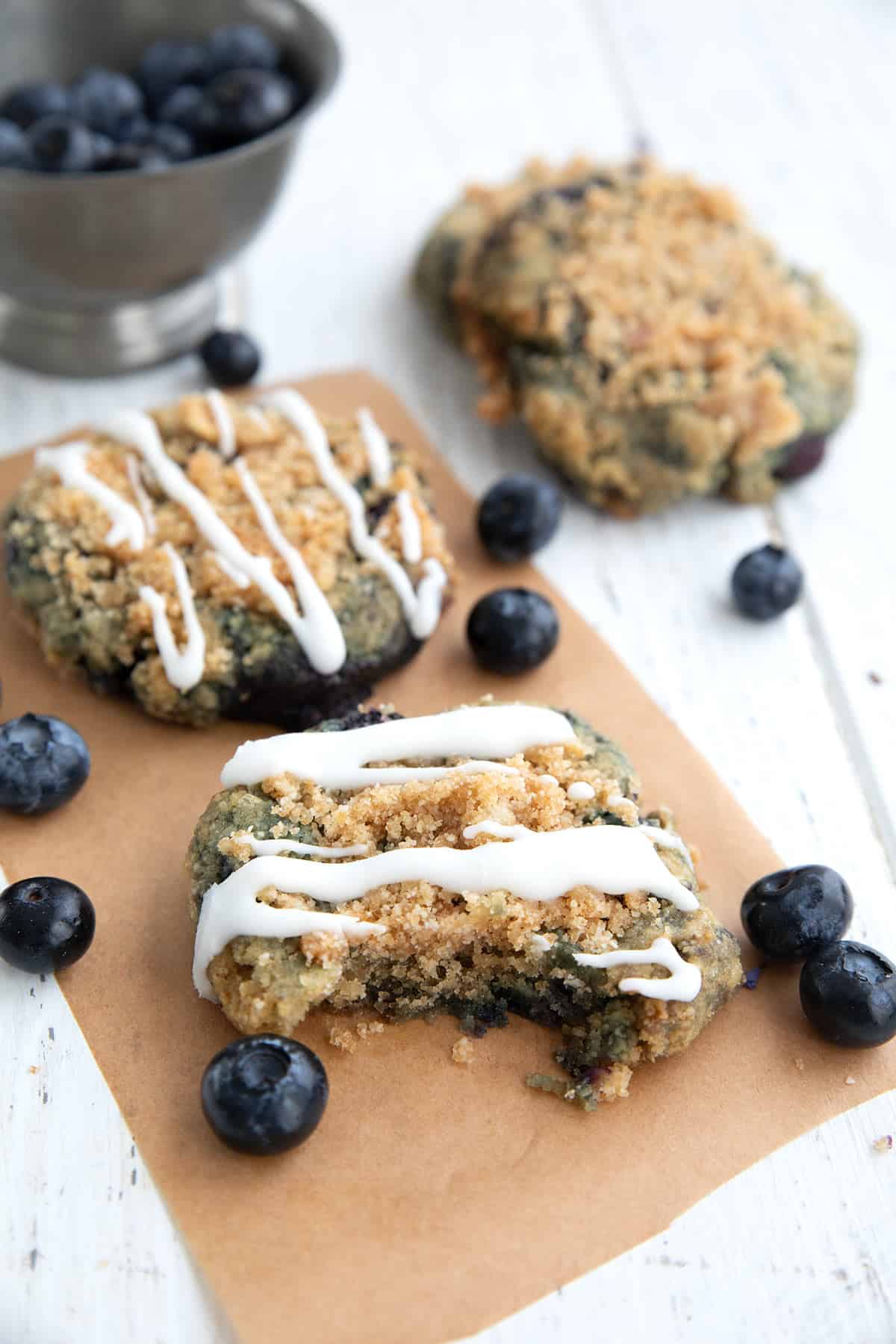 Keto blueberry muffin cookies on a piece of parchment paper with a bite taken out of one.