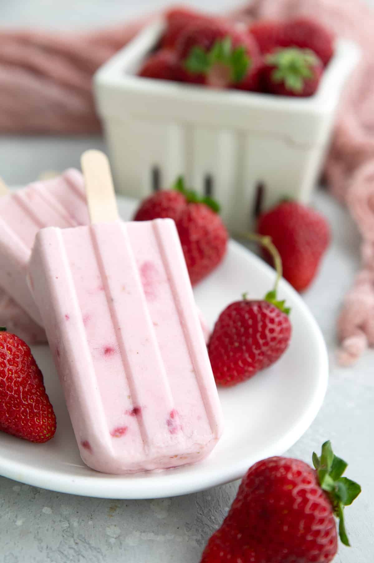 Keto Strawberry Popsicles on a white plate with strawberries in the background.