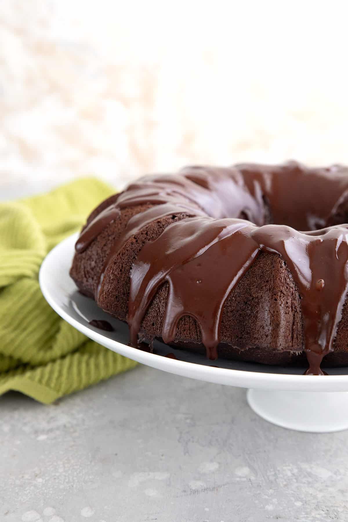 Keto Chocolate Bunt Cake with chocolate glaze on a white cake platter.