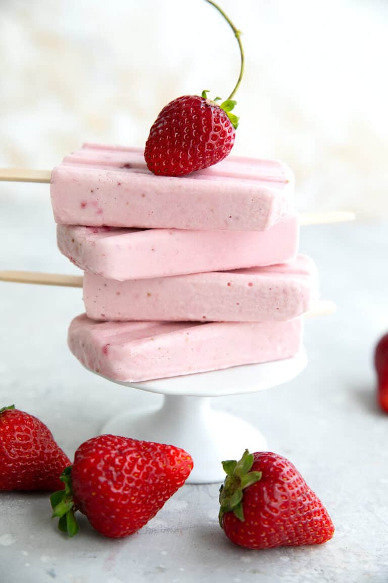 A stack of strawberry keto popsicles on a white cupcake stand, with a strawberry on top.