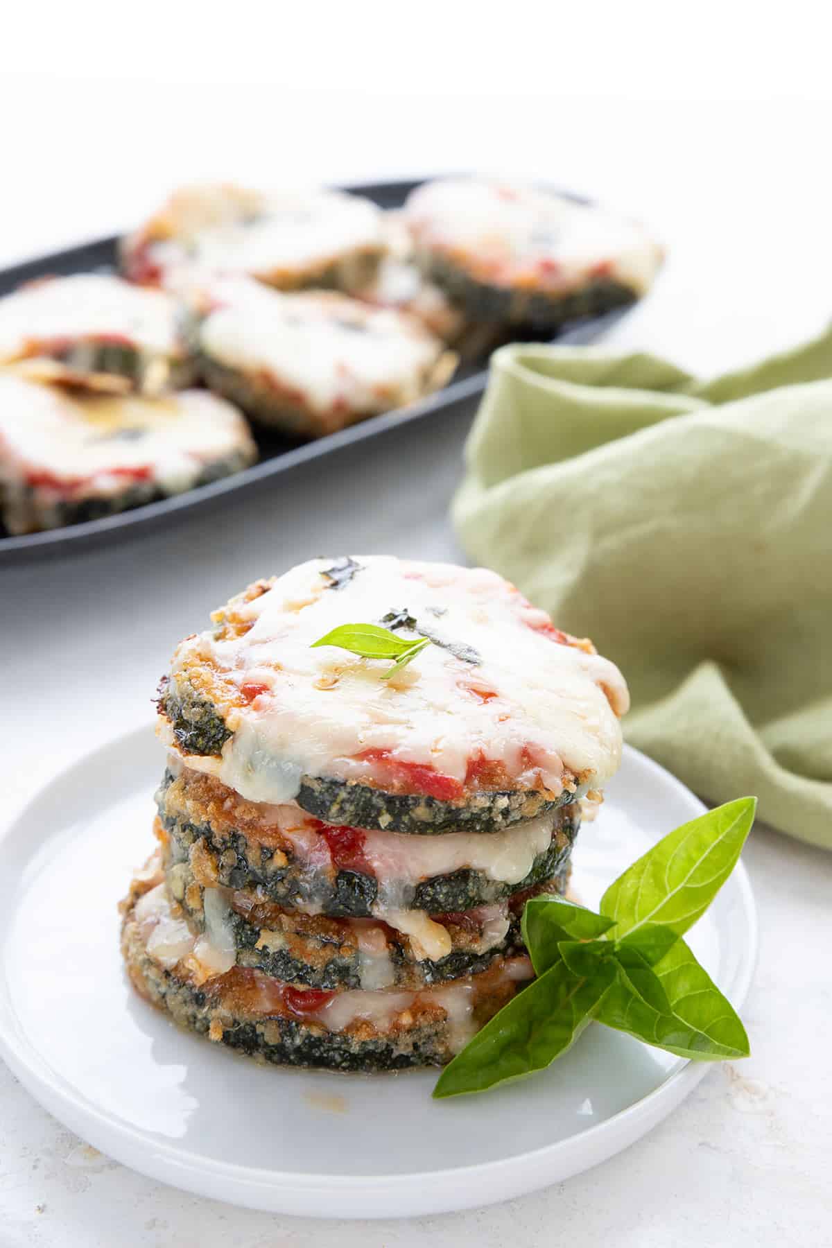 Zucchini Parmesan stacked up on a white plate with a green napkin in the background.