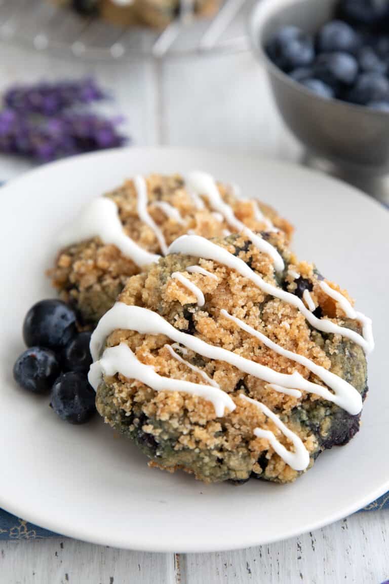 Two keto blueberry cookies on a white plate with fresh berries.