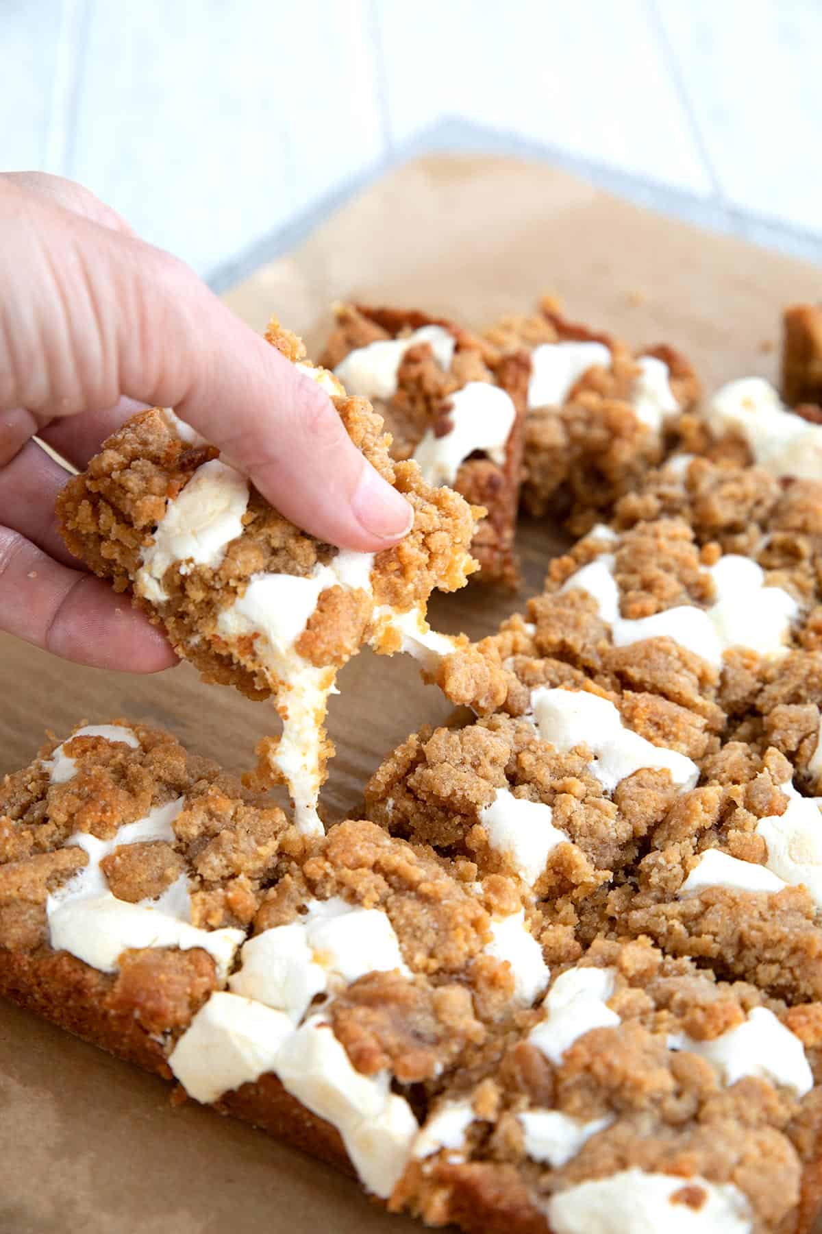 A hand pulling a Keto Fluffernutter Bar away from the pan of bars, with gooey sugar free marshmallows.