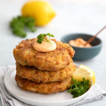 A stack of keto crab cakes on a white plate with lemon and parsley in the background.