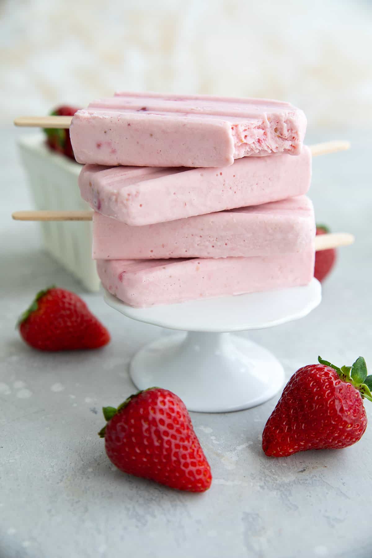 A stack of Keto Strawberry Cheesecake Popsicles on a white cupcake stand, with a bite taken out of the top one.