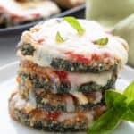 A stack of keto zucchini parmesan on a white plate with a sprig of basil.