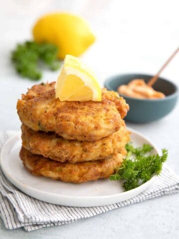 A stack of keto air fryer crab cakes on a plate with a slice of lemon on top.