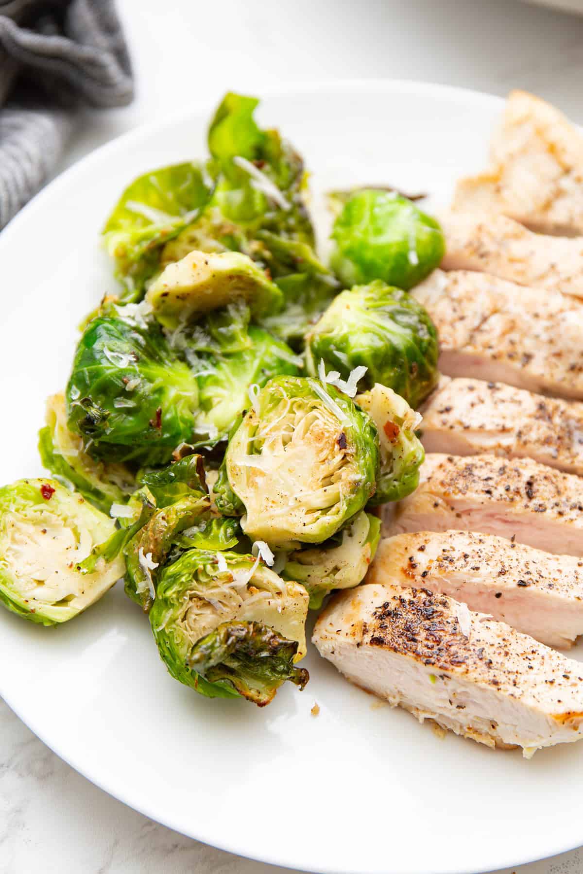Air Fryer Brussels sprouts on a white plate with chicken breast.