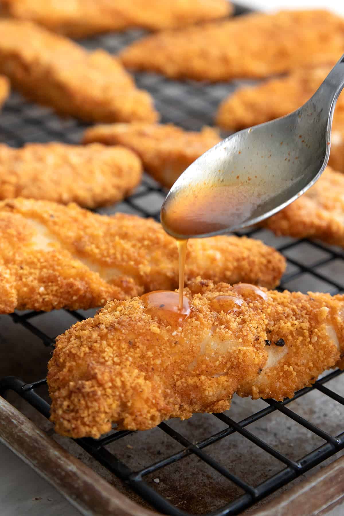 A spoon drizzling hot honey glaze over keto chicken tenders.